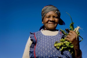 A woman holds up some of the vegetables she has grown in a garden in Cape Town, South Africa. © Kate Holt/Africa Practice