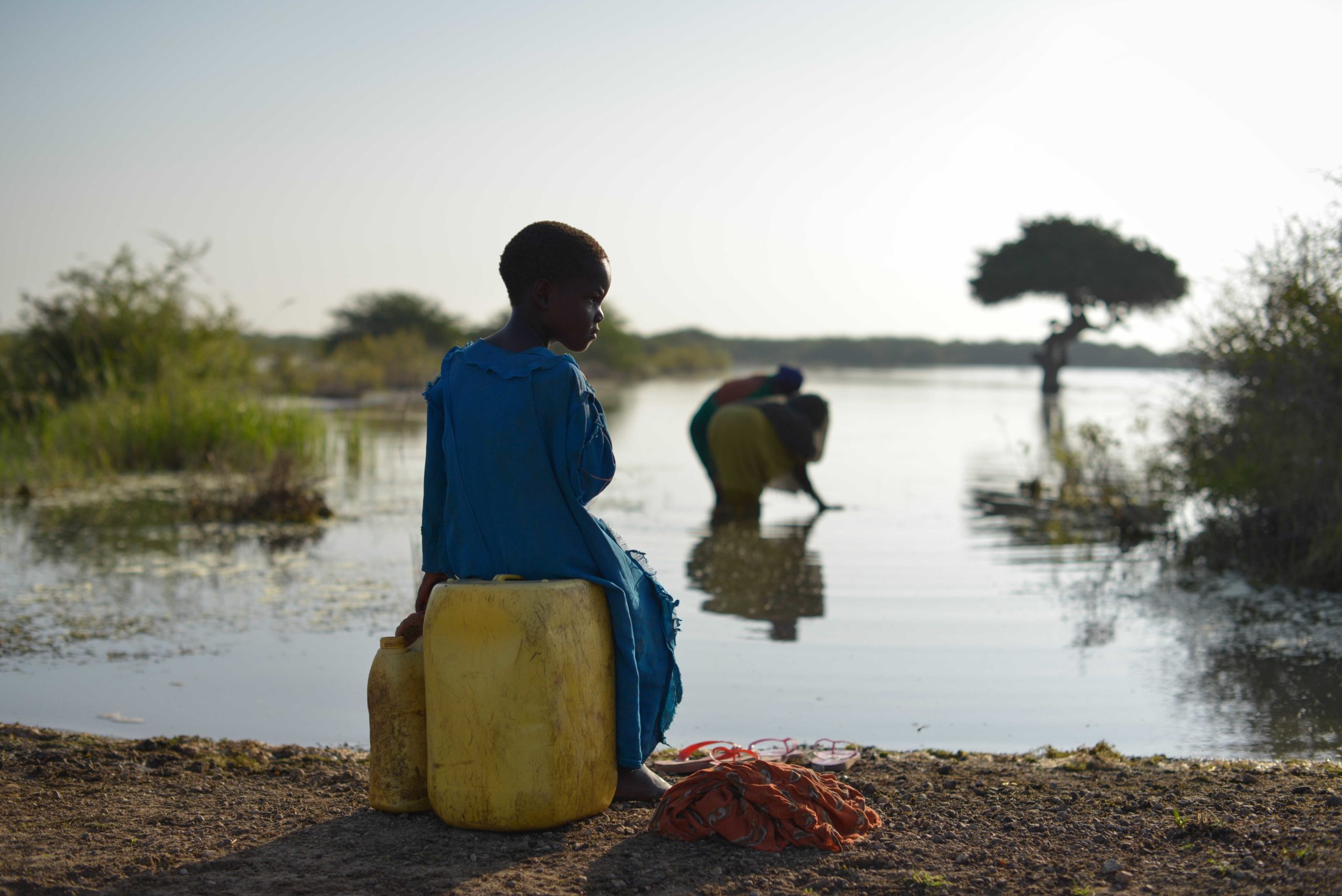 A young girl sits on a jerry can, as her mother fills up another with water, near the town of Jowhar, Somalia, on December 15. The area around Jowhar has experienced large amounts of flooding this year, completely blocking off the town from main roads and forcing thousands to flee their homes and seek shelter on higher ground. AU UN IST PHOTO / Tobin Jones